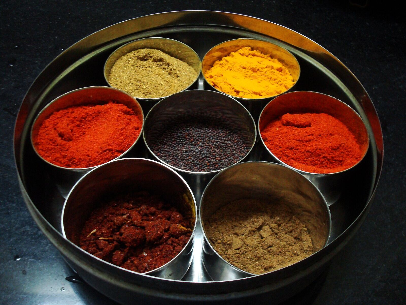 Such set of spices is quite common in an Indian household. (Going clockwise)Yellow on top is Turmeric, red to its red chilli powder, grey-brownish is Garam Masala, dark red is ginger-garlic-chilli dry masala, red is again red chilli powder, dark brown is corriender seeds and cumin seeds powder. At centre are black mustard seeds.